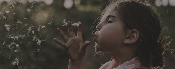 Young girl blowing a dandelion